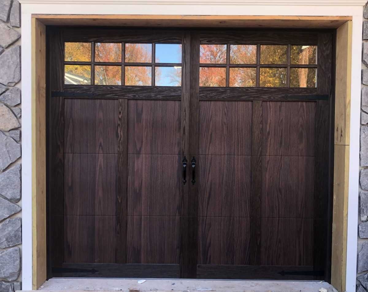 Dark wooden double garage door with small glass panes at the top in a stone frame