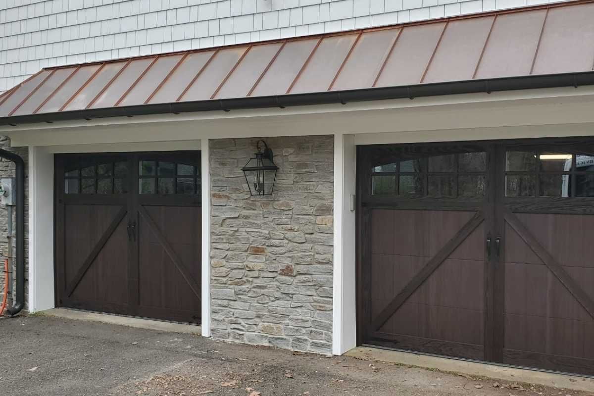 Two brown garage doors flanking a stone wall under a metal roofline