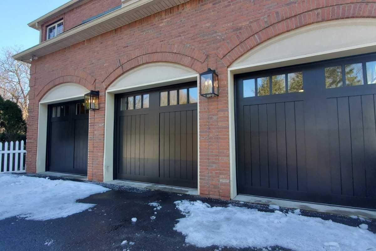 Brick house with three black garage doors and snow on the driveway