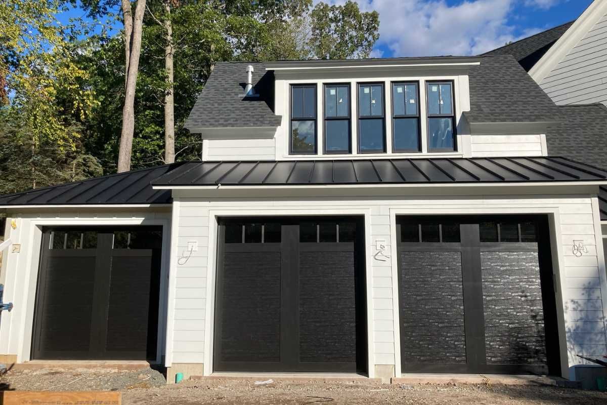 Modern black-and-white house exterior with three garage doors and a dormer window