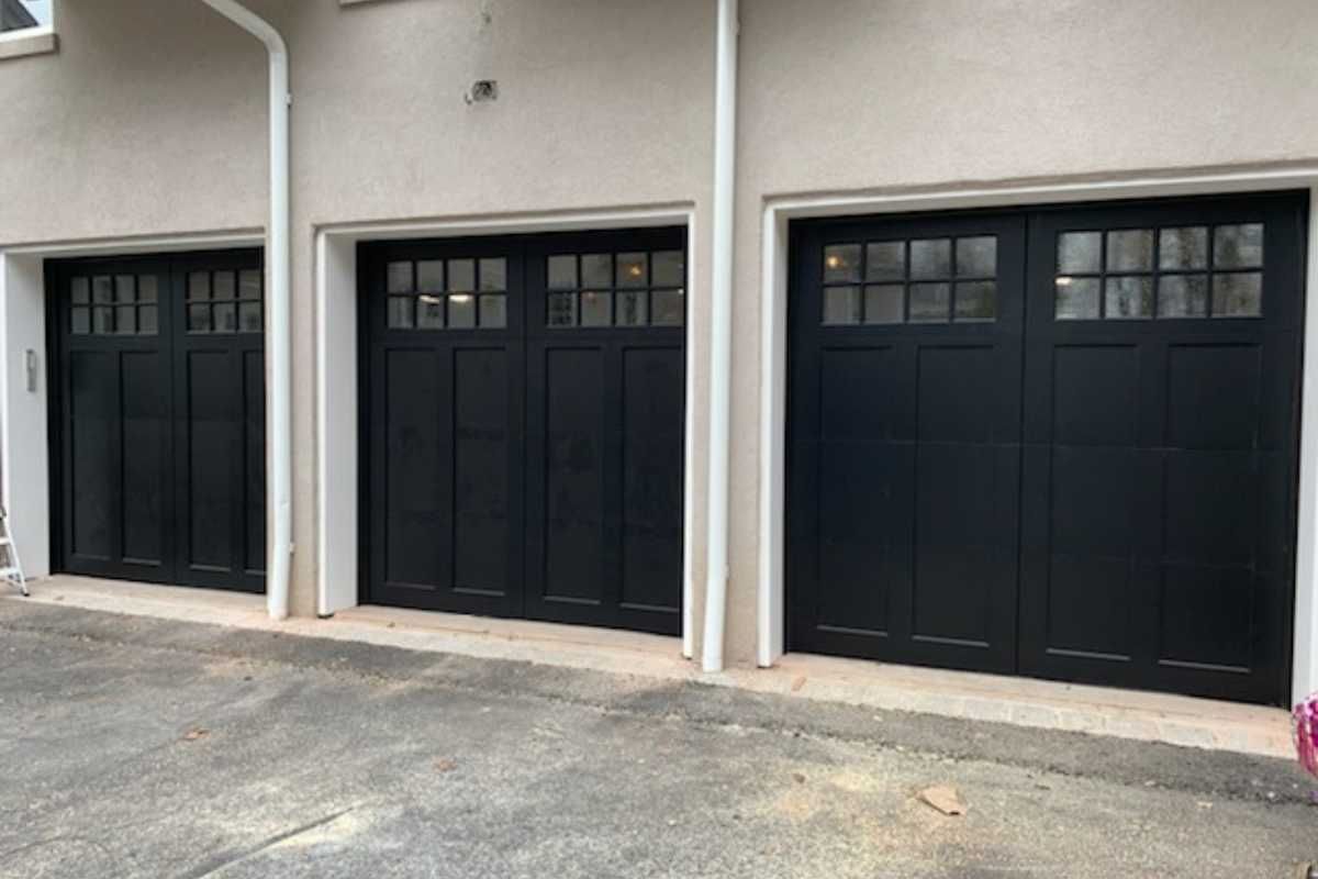 Row of three black garage doors on a beige exterior wall with concrete driveway in front