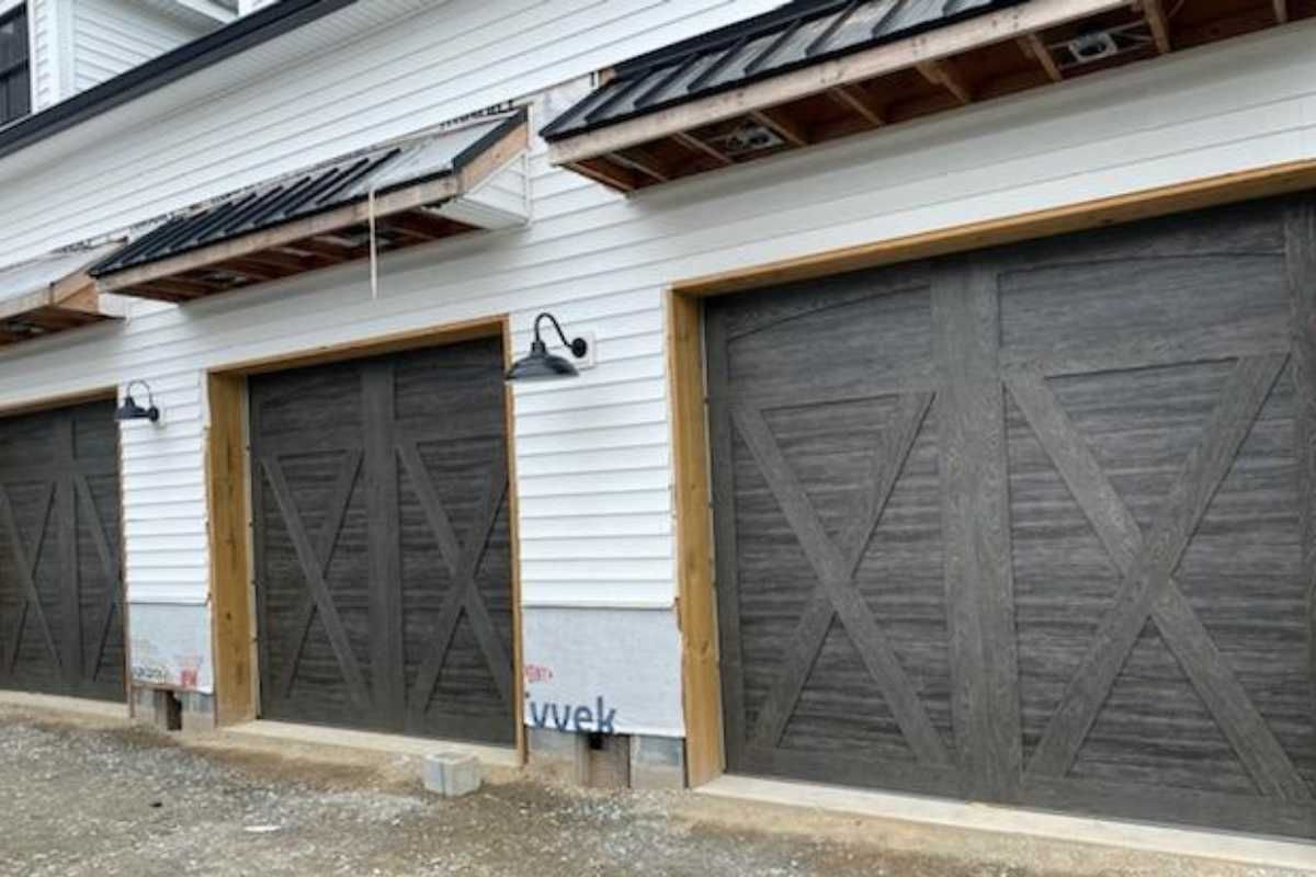 Two dark wooden garage doors on a white-sided building with stone base and solar panels above