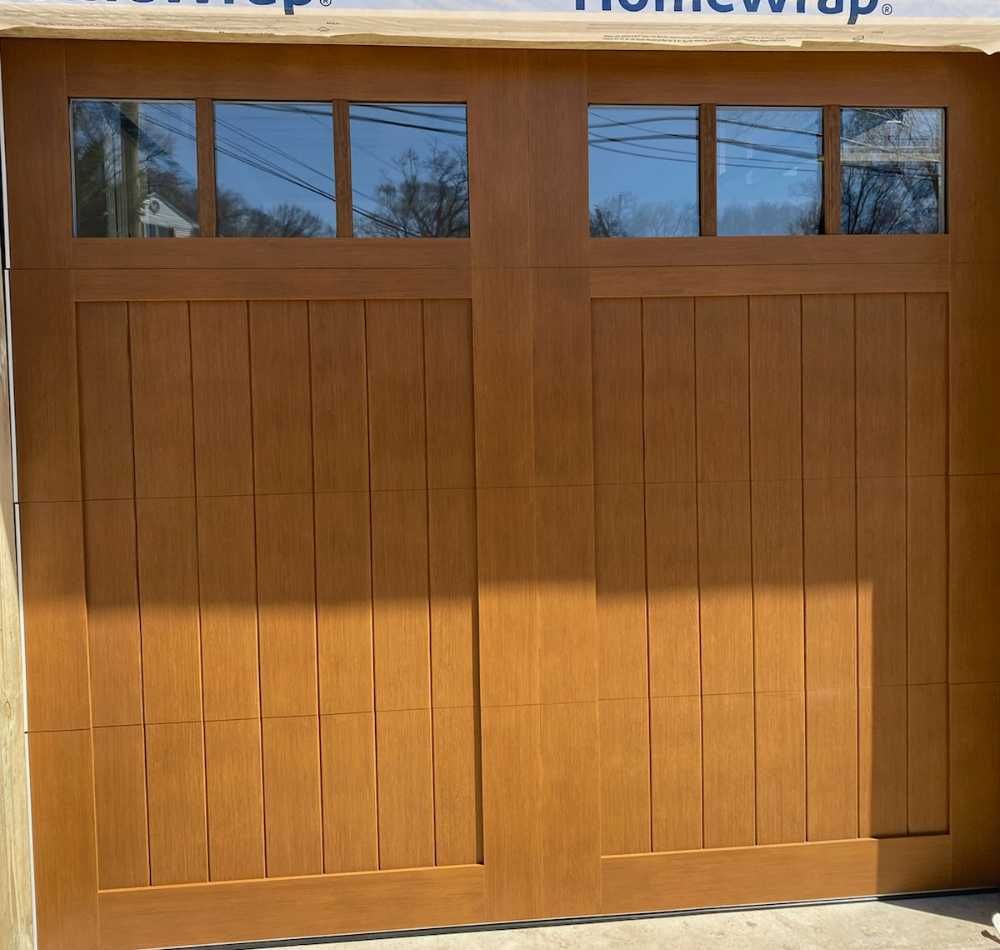 Wooden garage door with four small upper windows, lit by sunlight