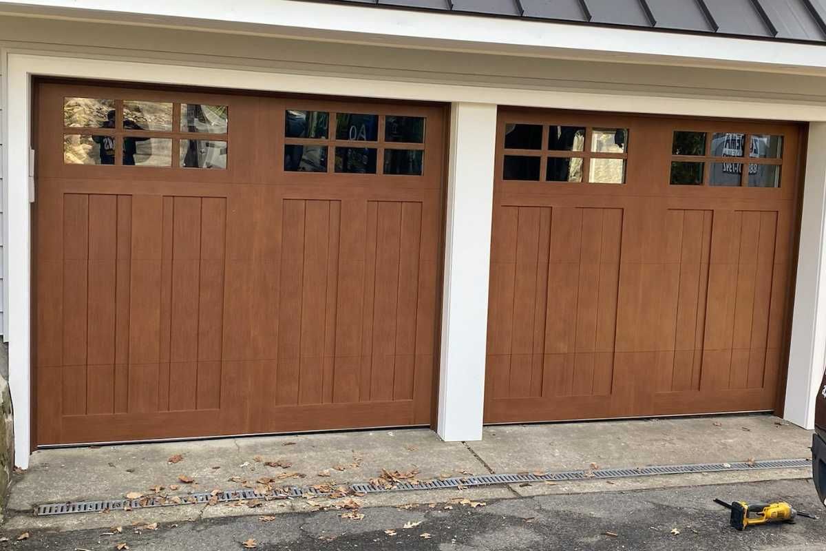 Two brown wooden garage doors with small windows above, separated by a white column.