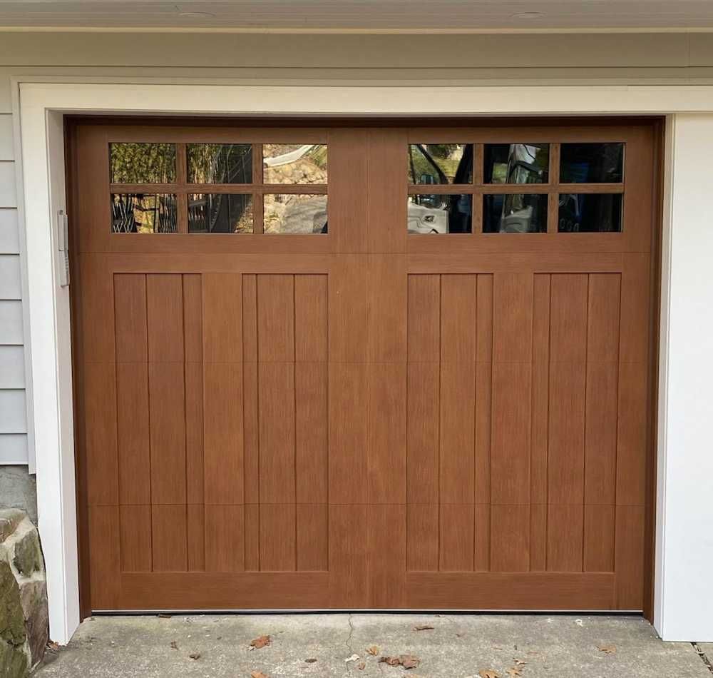 Wooden garage door with rectangular windows at the top, set in a light-colored house exterior.