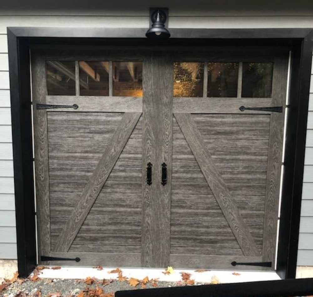 Gray barn-style double garage door with black trim and small windows at the top