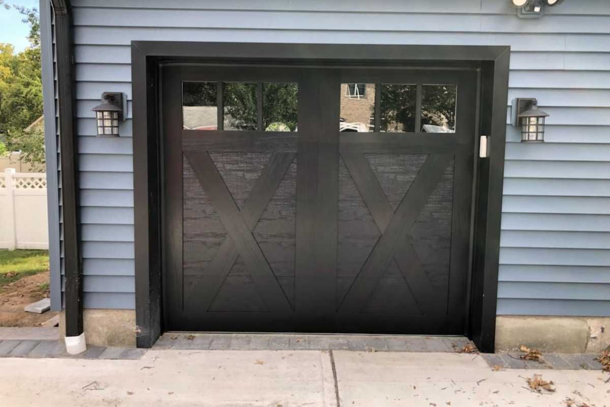 Black garage door with X-pattern panels on a blue house exterior