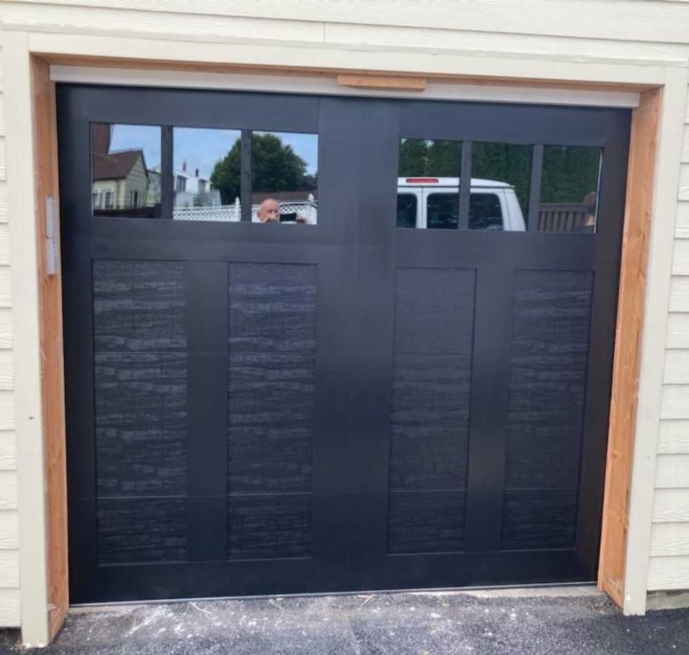 Black garage door with small windows in a tan house exterior
