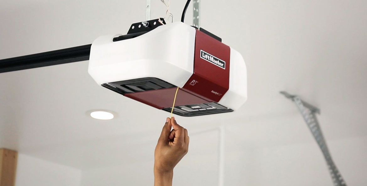 Hand pulling the emergency release cord on a red-and-white garage door opener.