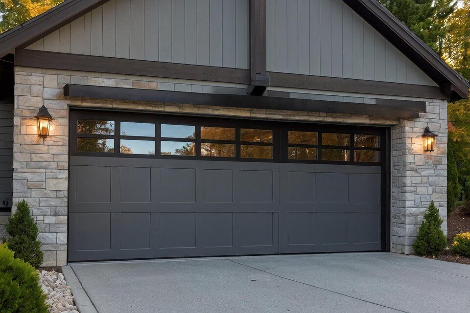 Modern gray garage with stone accents, warm lantern lights, and a concrete driveway