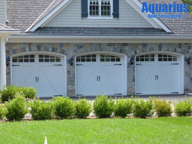 White three-car garage with dormer windows and landscaped lawn, labeled Aquarius Downspouts in the corner