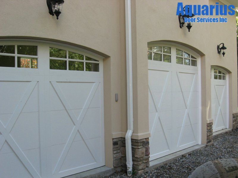 Two white garage doors with arched windows on a beige stucco building