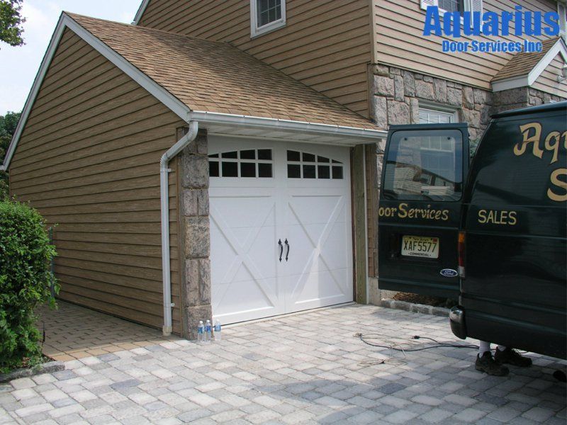 White double garage door beside a black service truck on a paved driveway next to a tan house