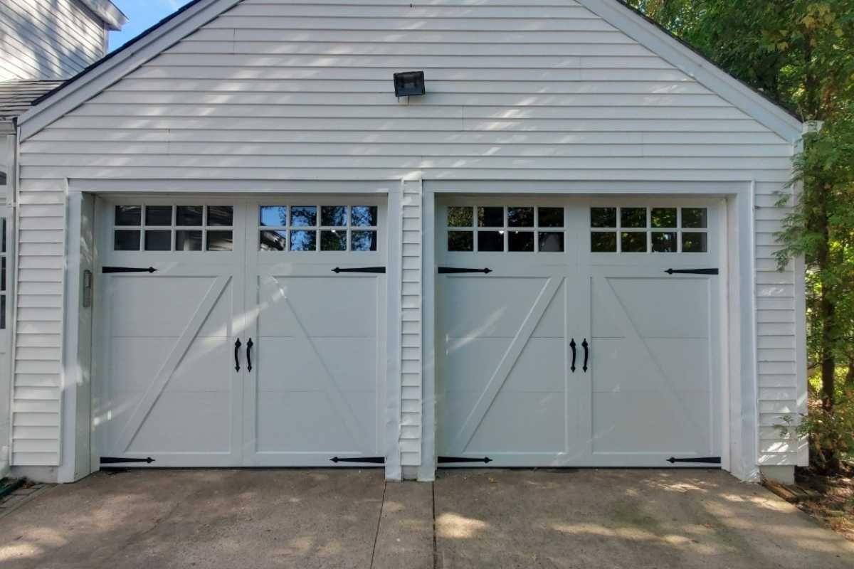 Two white garage doors on a gray-sided detached garage with small window panes above each door