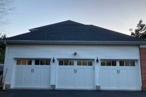Three white garage doors on a suburban house with gray siding and a dark roof