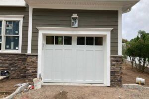 Front exterior of a house with a white double garage door and stone-and-beige siding.