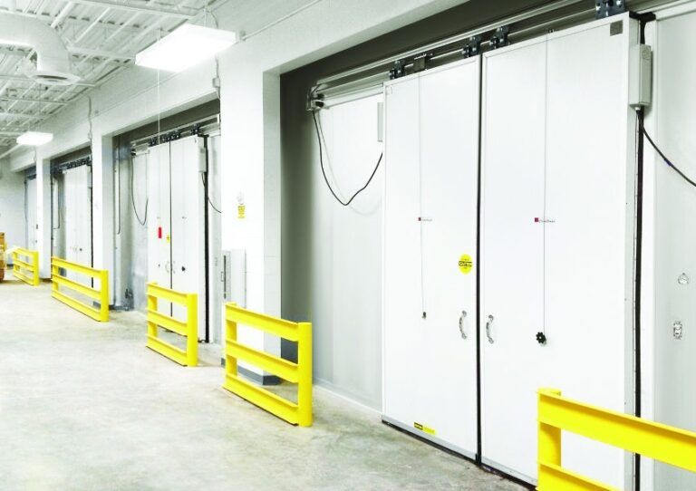 Industrial hallway with white doors and bright yellow safety barriers along the wall