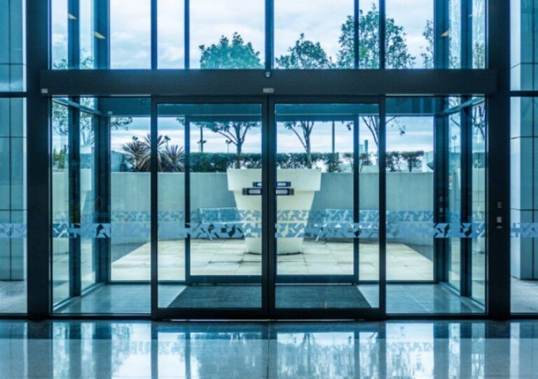 Glass-walled modern lobby with reflective floor and view of outdoor courtyard