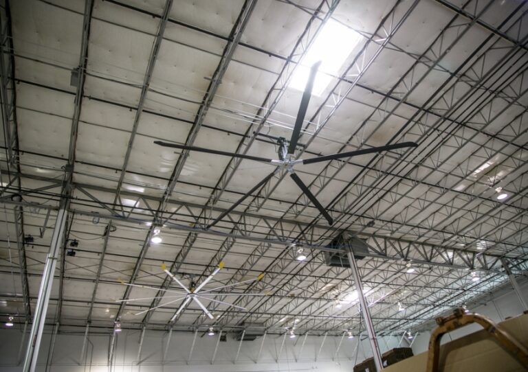 Interior of a large industrial warehouse ceiling with metal trusses and bright overhead lights