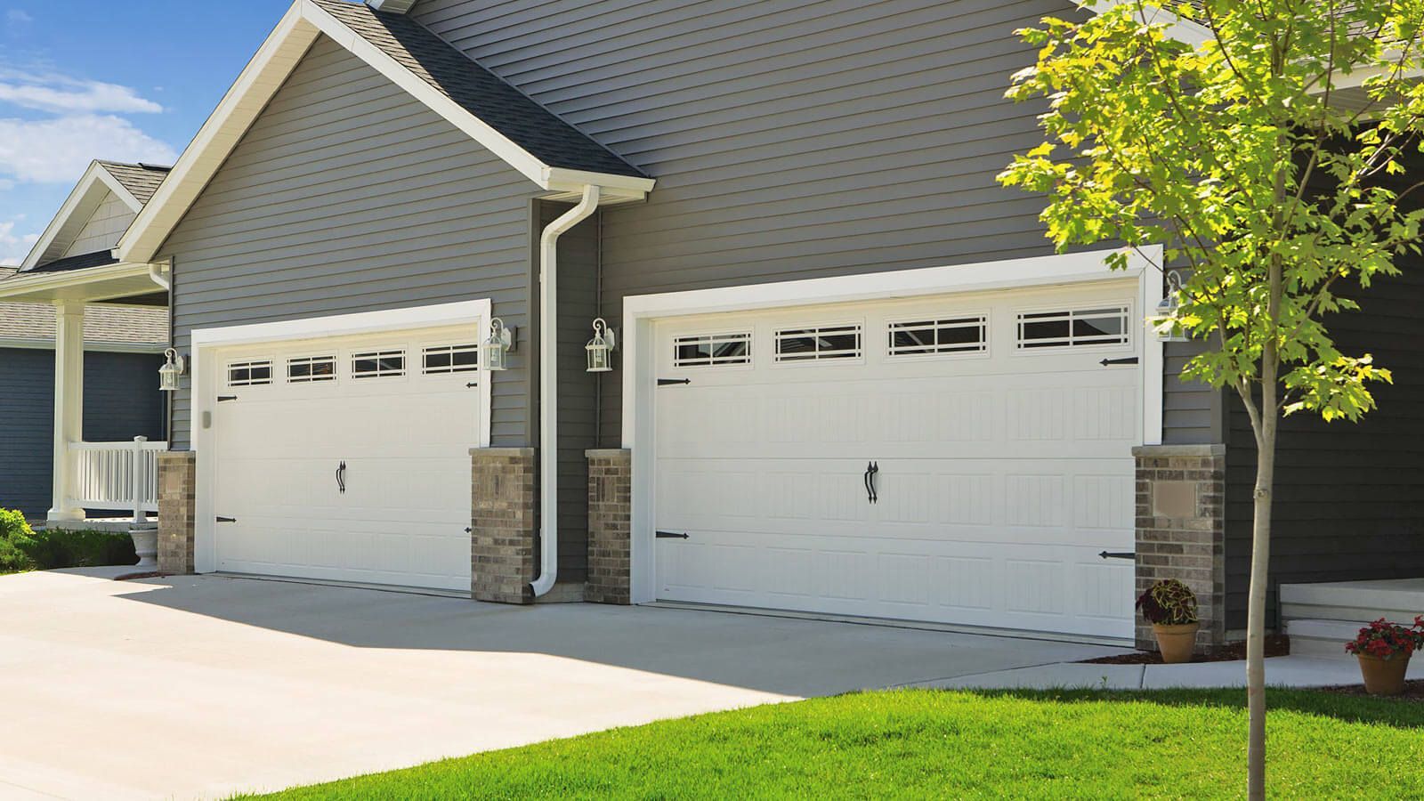 Two white garage doors on a gray house with stone trim and a green lawn in front