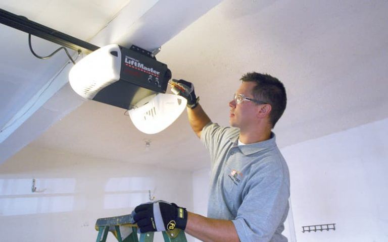 Man installing a garage door opener on a ceiling with a ladder below