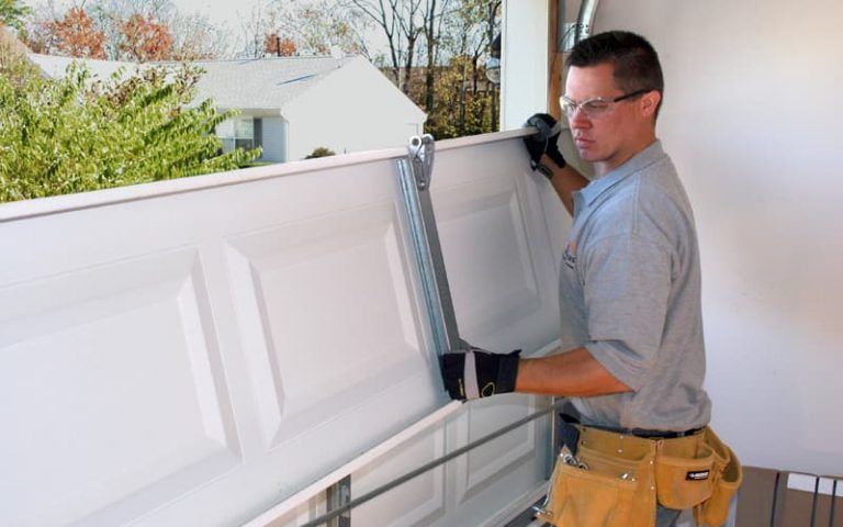 Worker installing a white garage door panel with tools on a sunny day