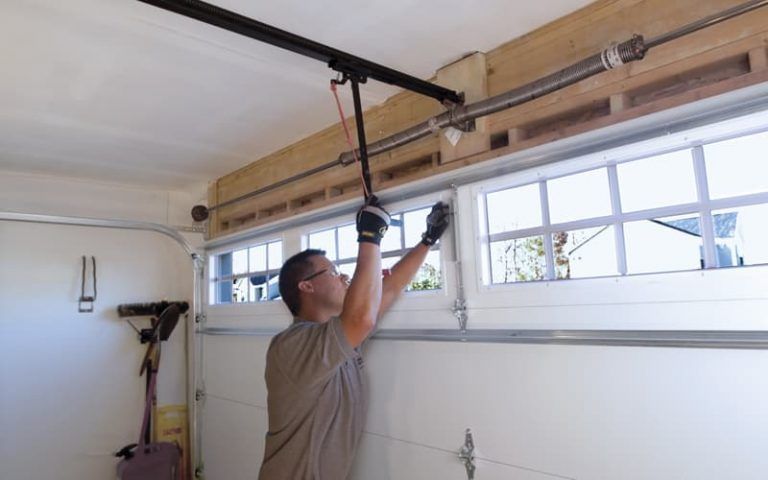 Man adjusting a garage door opener rail near the ceiling in a garage