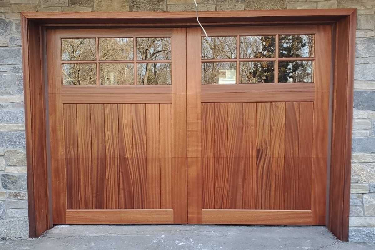 Wooden double garage doors with glass panes above, set in a stone wall.