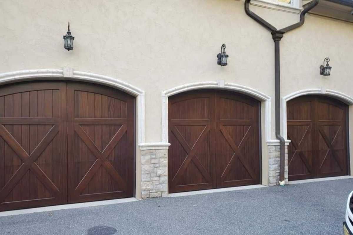 Three brown wooden garage doors on a stucco building with stone trim and wall lanterns