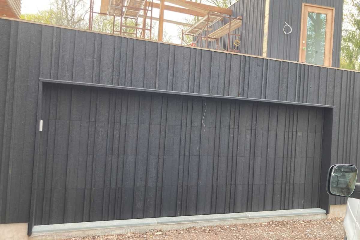 Large black wooden gate and fence in front of a house under construction