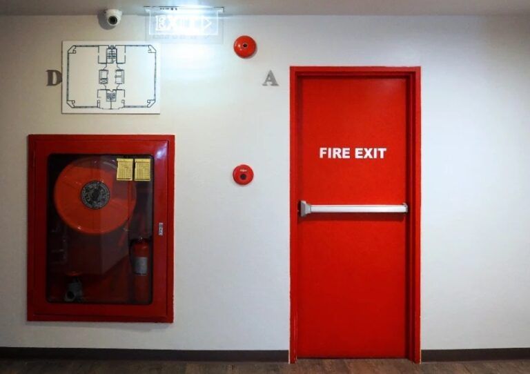 Wall with fire hose cabinet and red FIRE EXIT door in a hallway.