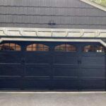 Black garage door beneath a gray shingled roof with small arched windows above.