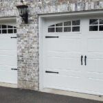 White garage doors set in a stone house exterior, with black handles and small window panes.