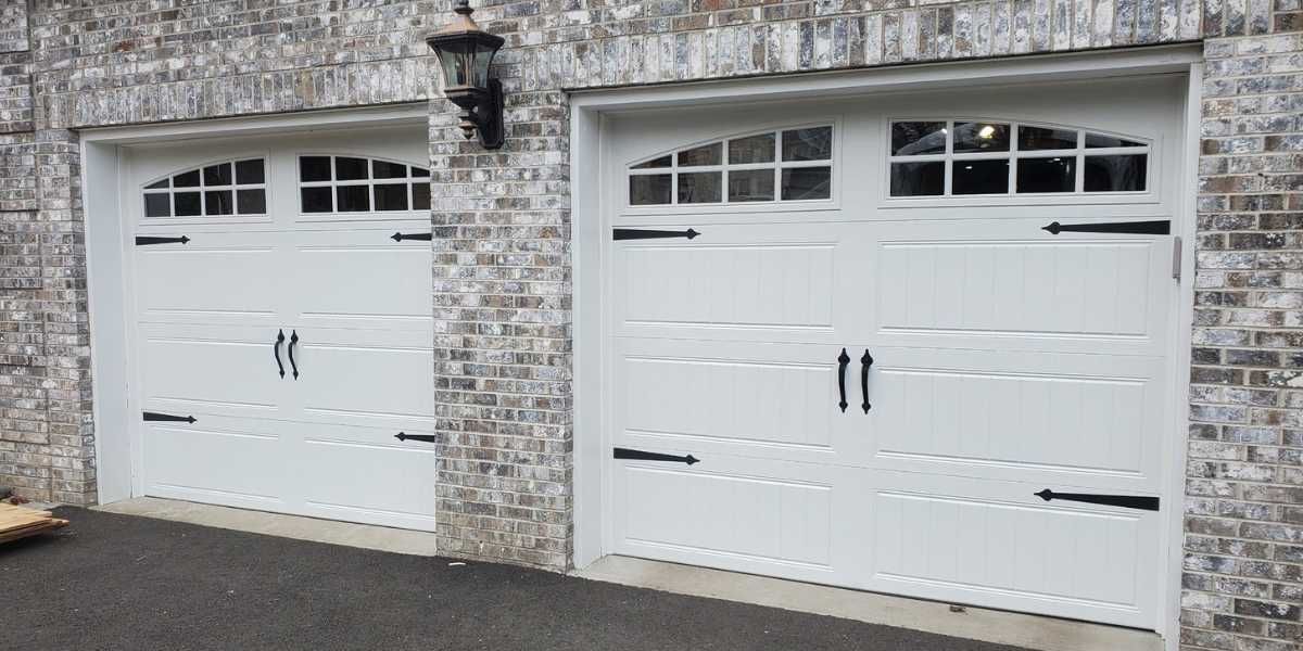 Two white garage doors with black handles on a stone house exterior