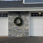 Front of a house with two garage doors and a wreath on the stone wall between them