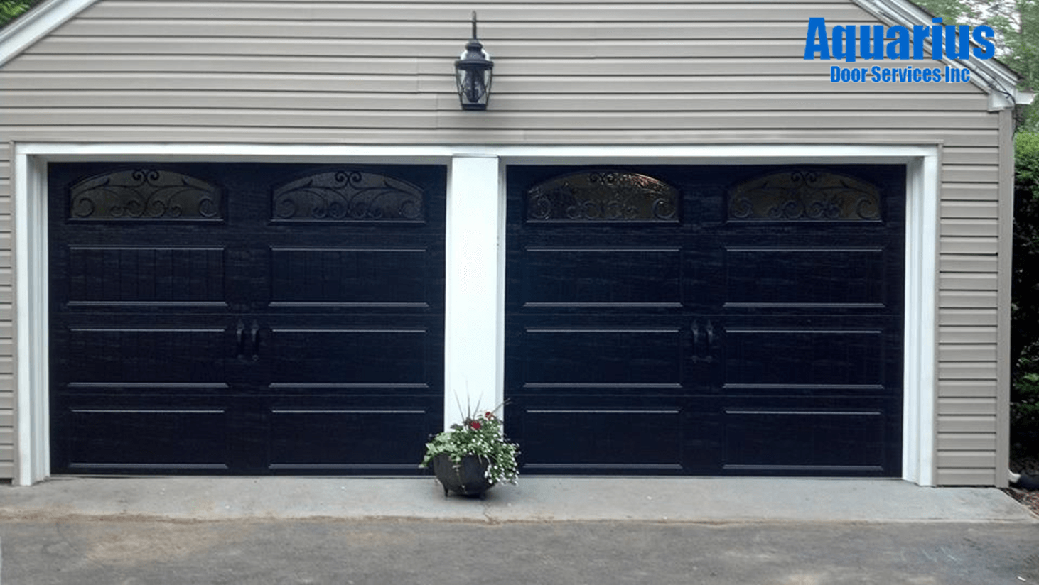 Two black garage doors on a gray building with a small potted plant in front