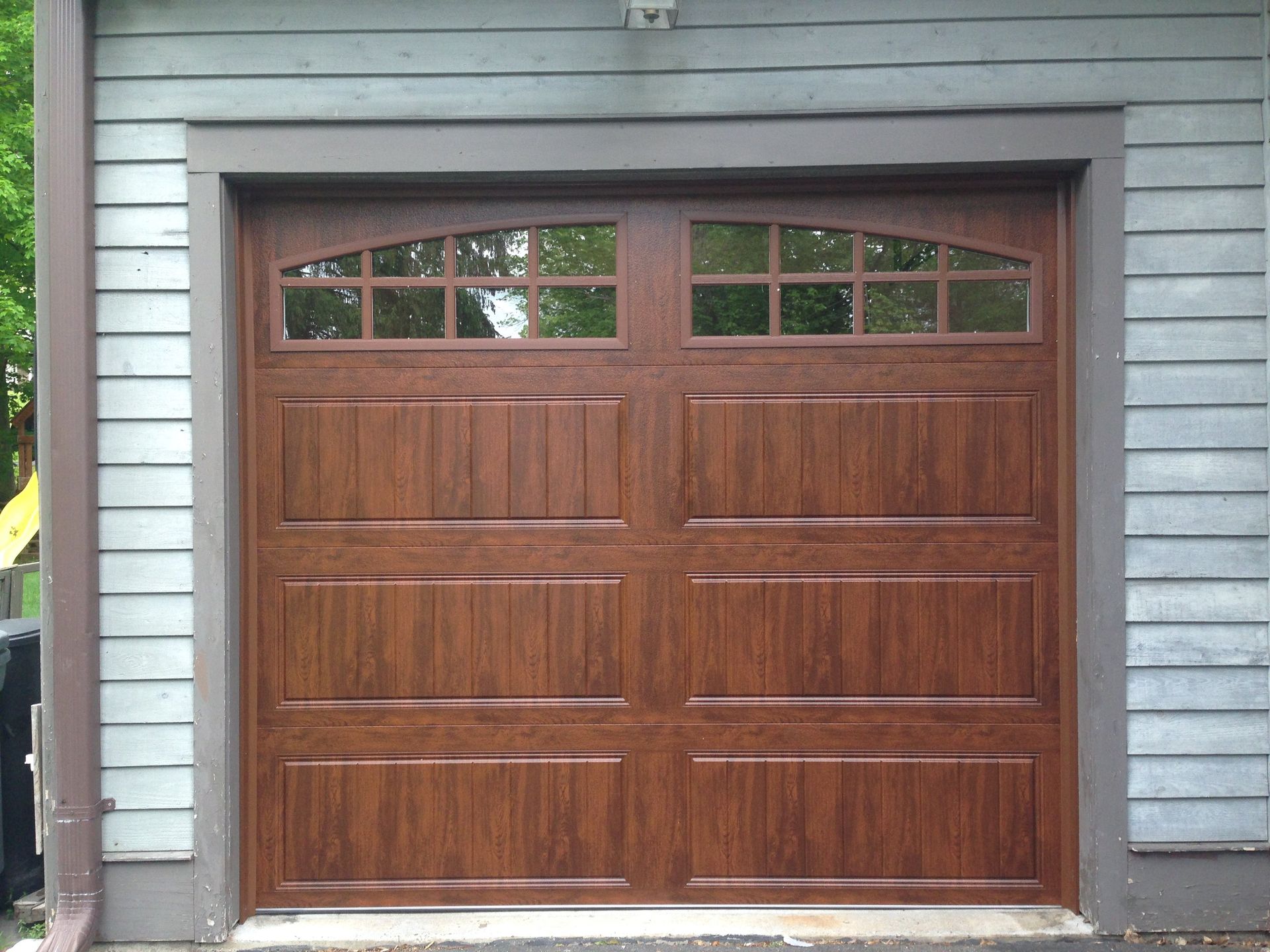 Wooden double garage door with arched windows in a gray-sided house exterior