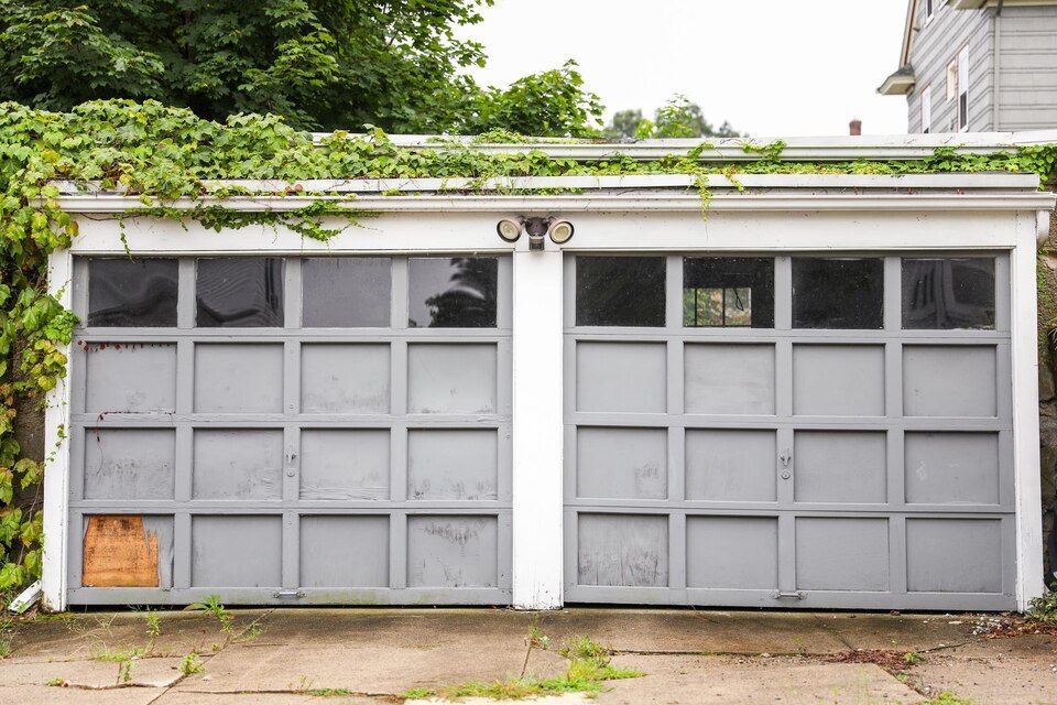 Gray double garage doors with small upper windows on a vine-covered house exterior