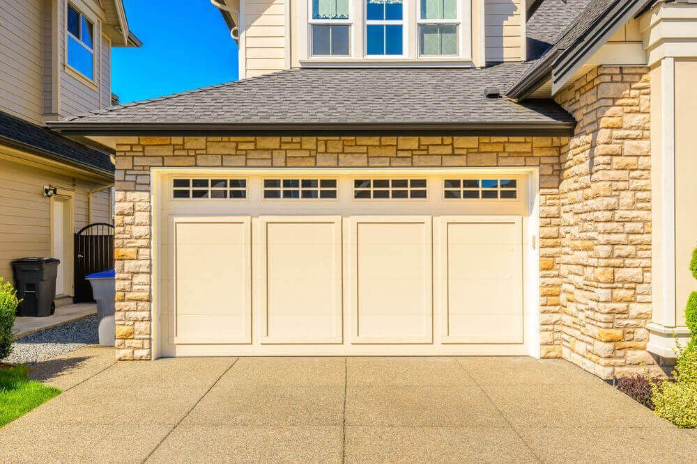 Beige double garage doors on a stone-faced suburban house with a concrete driveway