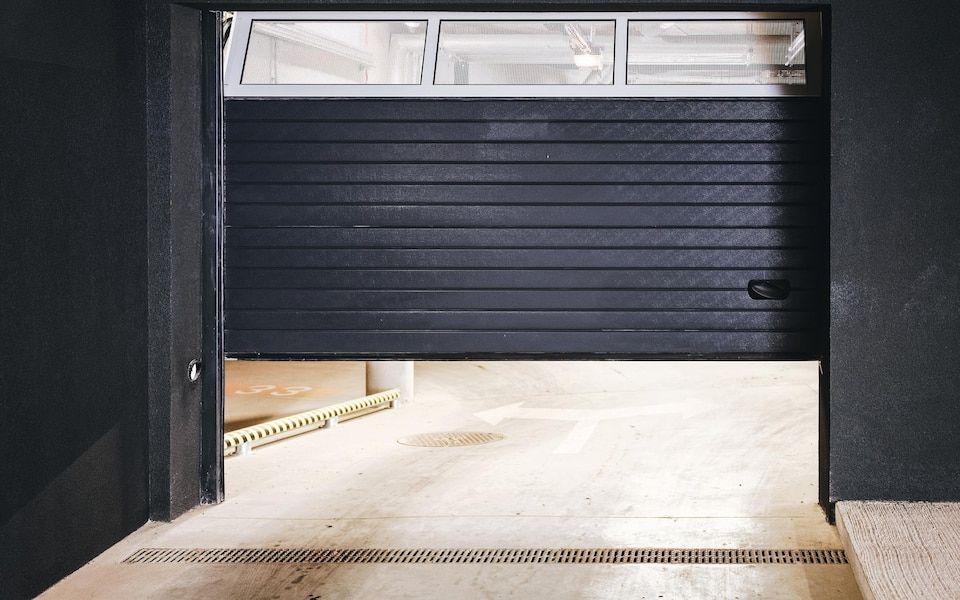 Partially open dark garage door with light concrete floor visible inside