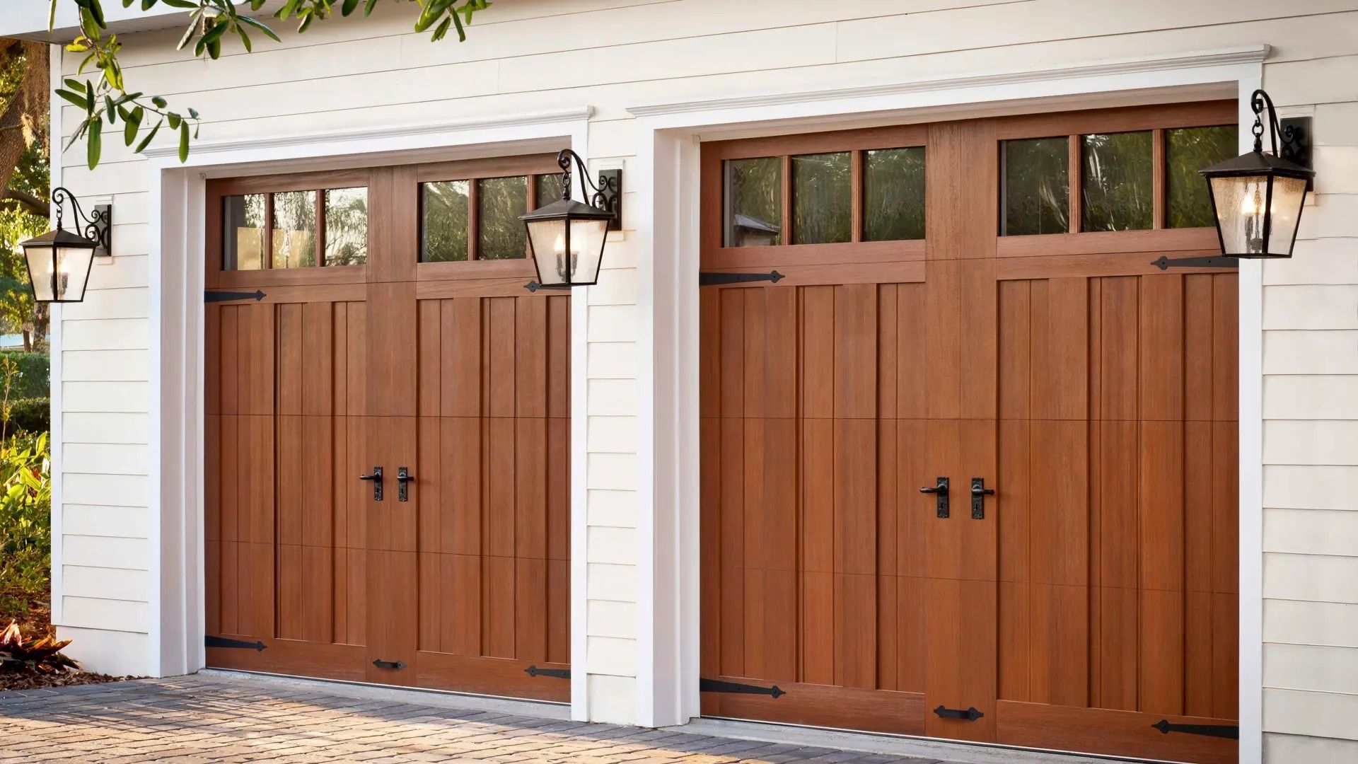Two wooden garage doors on a white house exterior with black lantern-style lights