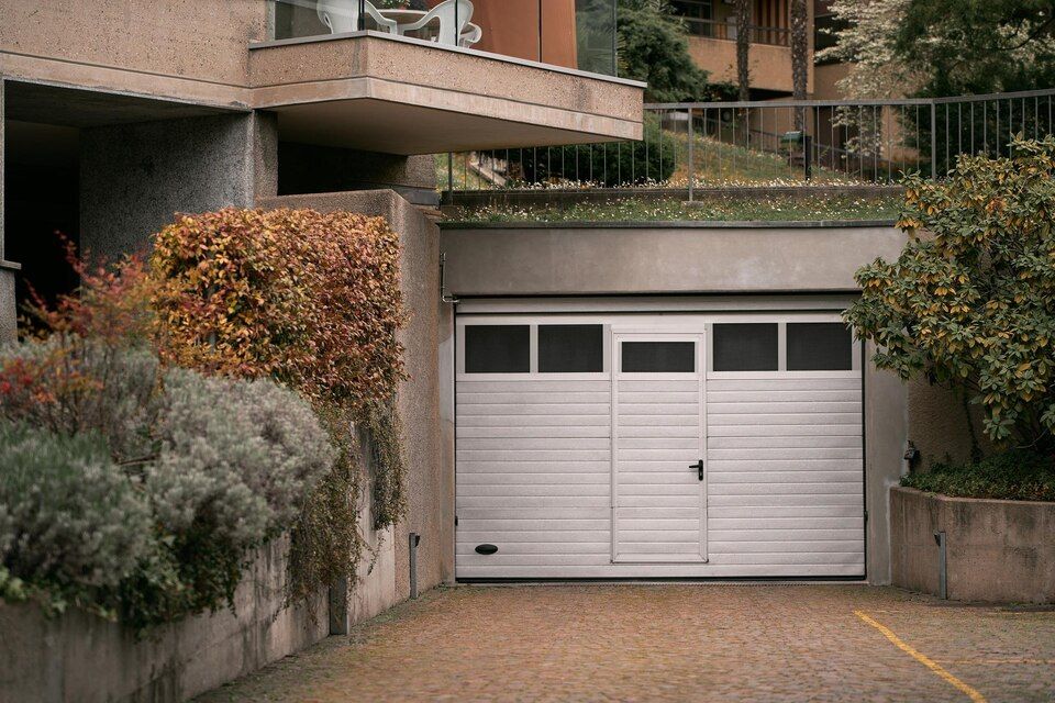 White garage doors beneath an apartment building entrance, framed by shrubs and concrete walls