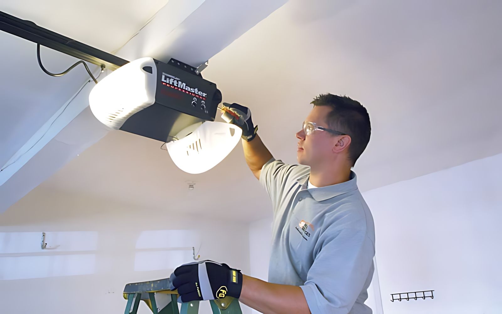 Technician installing a garage door opener on the ceiling with a ladder nearby