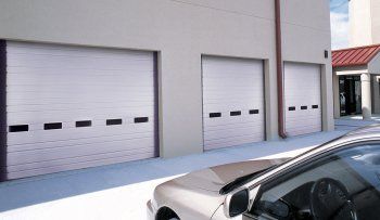 Row of gray roll-up garage doors on a commercial building, with a car in the foreground