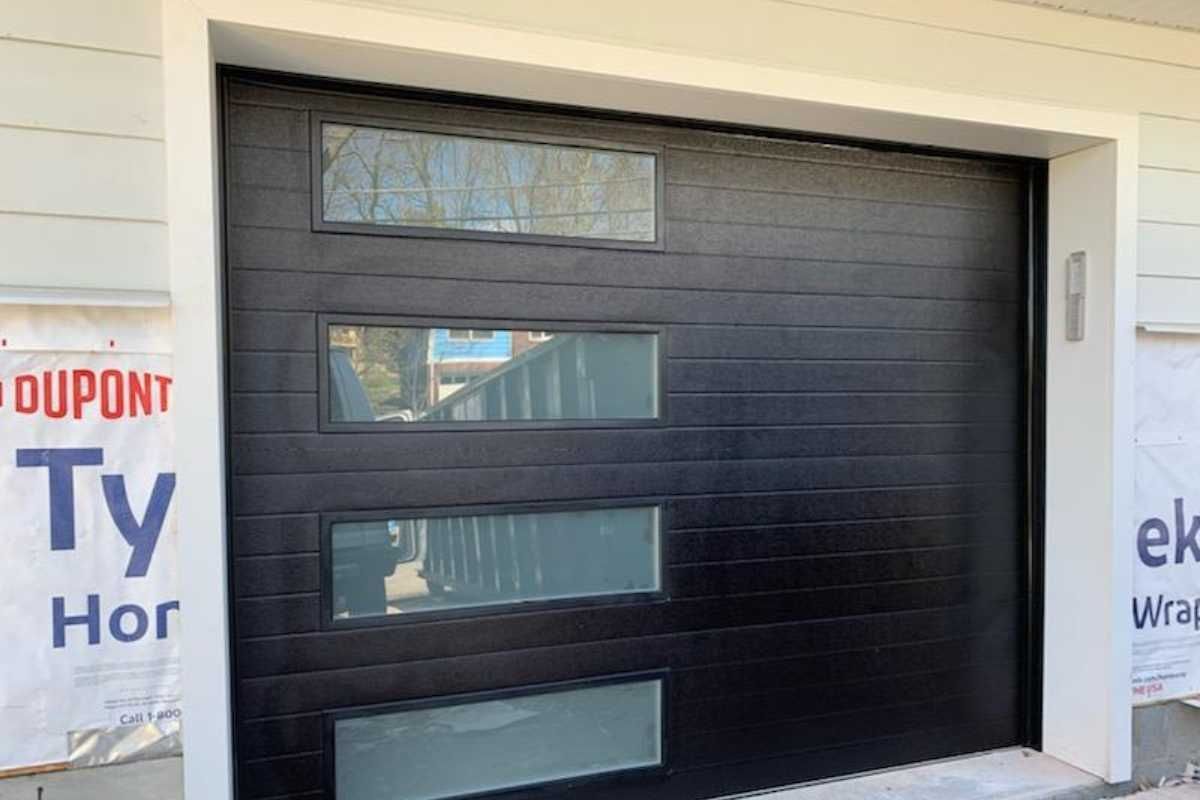 Black garage door with four narrow windows in a white exterior wall under construction
