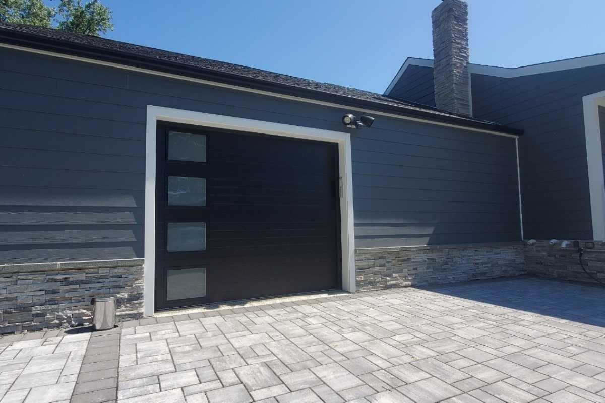 Modern house exterior with open garage and gray siding, viewed from a paved driveway
