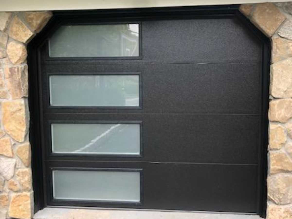Modern black garage door with four frosted glass panels, framed by stone siding