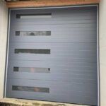 Closed gray metal garage door with four horizontal rectangular windows in a beige frame