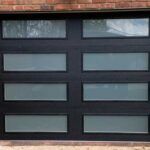 Black garage door with eight frosted rectangular windows beneath a brick wall