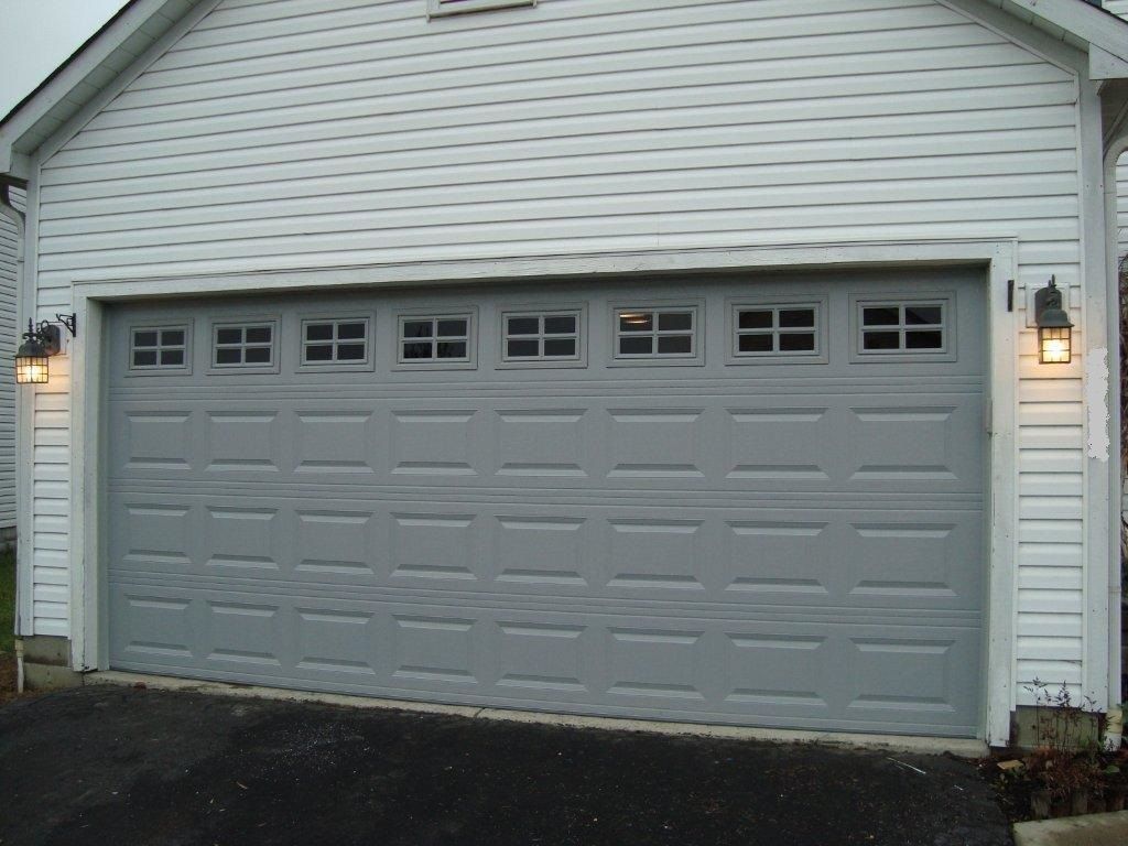 Gray two-car garage with white siding and lit wall lanterns at dusk